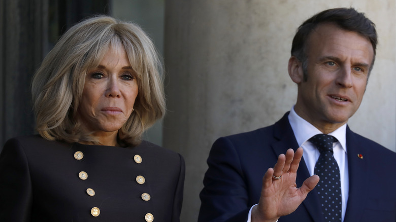Emmanuel Macron waving while Brigitte Macron stands beside him