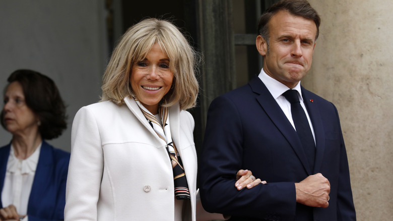 Emmanuel and Brigitte Macron smiling and walking