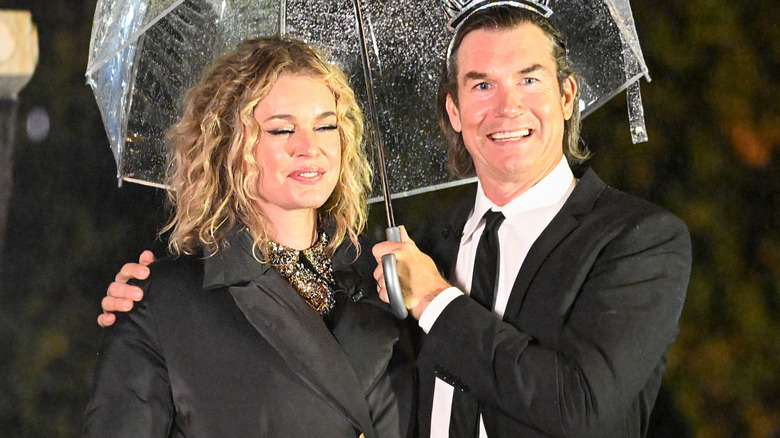 Jerry O'Connell with his arm around Rebecca Romijn while he holds an umbrella