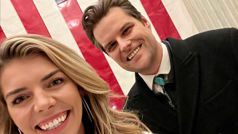 Ginger and Matt Gaetz take a selfie, smiling in front of an American flag