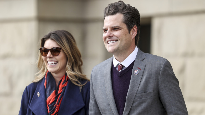 Matt Gaetz in a grey suit and Ginger Luckey (now Gaetz) in a navy coat smiling a rally in effort to vote Liz Cheney out of office