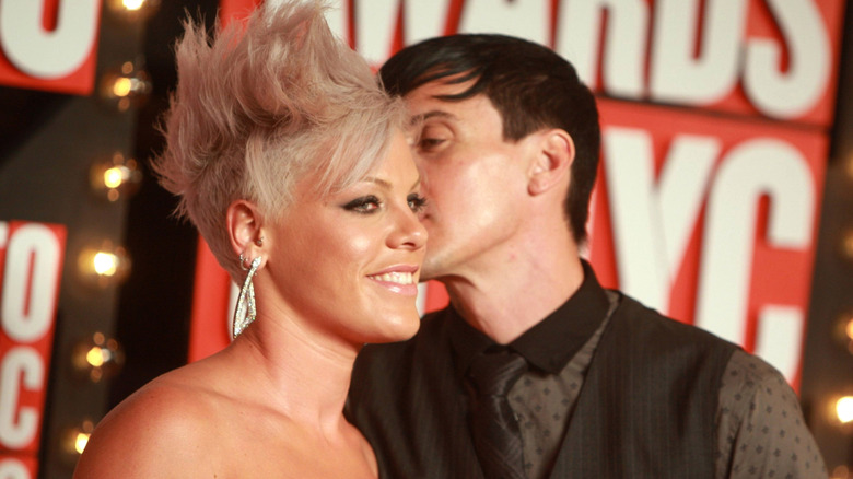 Pink with blonde faux hawk being kissed on cheek by Carey Hart in black dotted shirt with black vest and tie