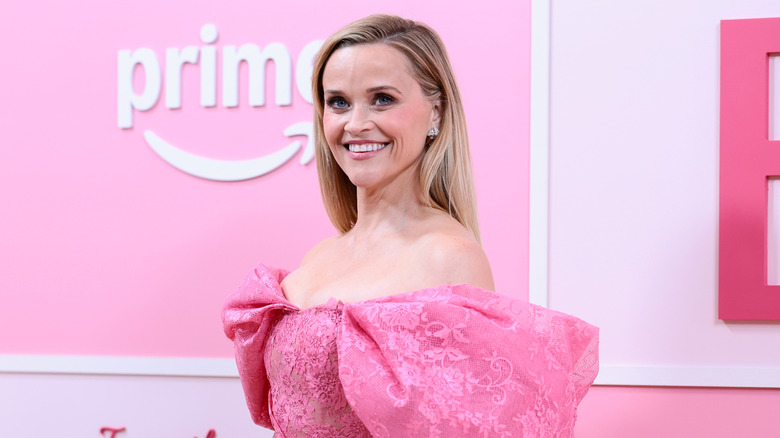 Reese Witherspoon posing on the red carpet for the Legally Blonde spin-off series Elle in a pink lacy dress with puffy sleeves