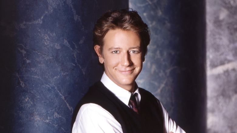 Judge Reinhold smiling while wearing a red tie, a black sleeveless sweater, and a white shirt