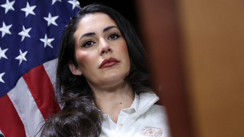 Anna Paulina Luna looking annoyed in front of an American flag