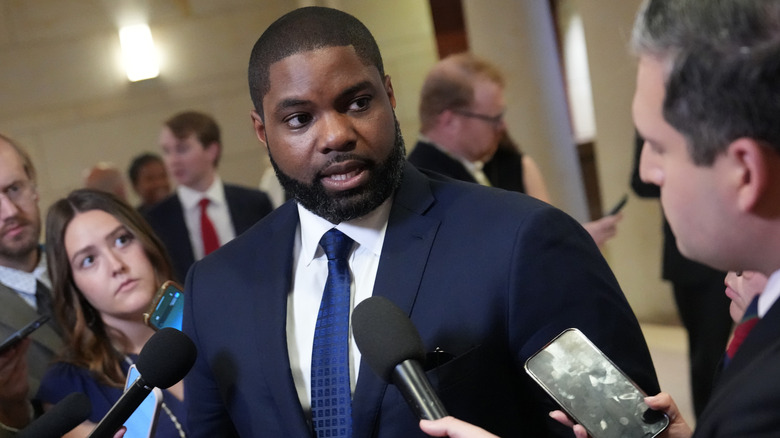 Tilted angle photo of Byron Donalds surrounded by press and microphones.