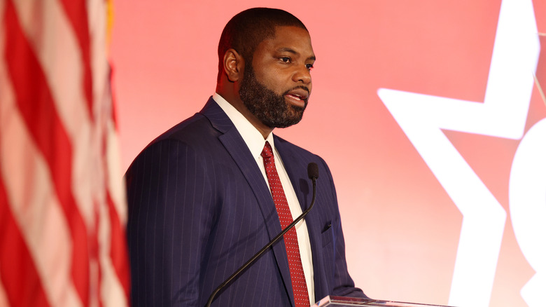 Rep. Byron Donalds in a blue suit behind a podium, talking.