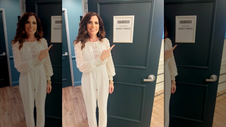 Nancy Mace in an all-white outfit pointing at a door that has her name on it.