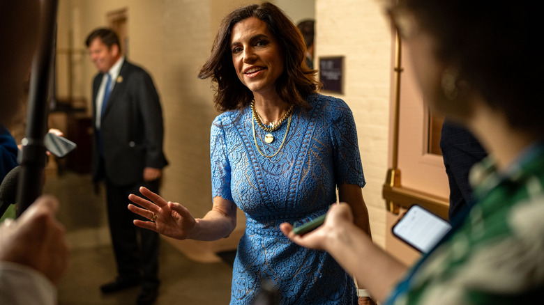 Nancy Mace with her hand raised in a blue dress as she talks to press.
