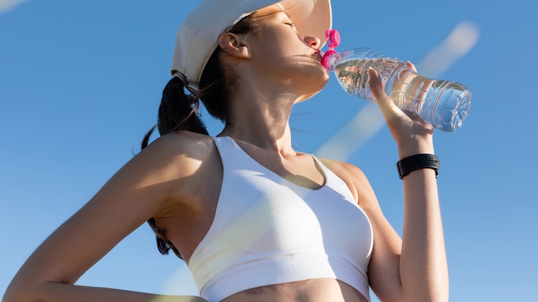 A woman drinking water while wearing a sports bra 