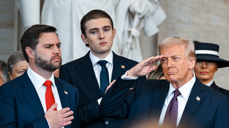 Donald Trump saluting next to JD Vance while Barron Trump stands behind him looking sad