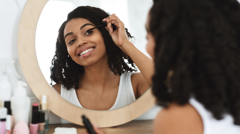 Woman applies mascara in the mirror 