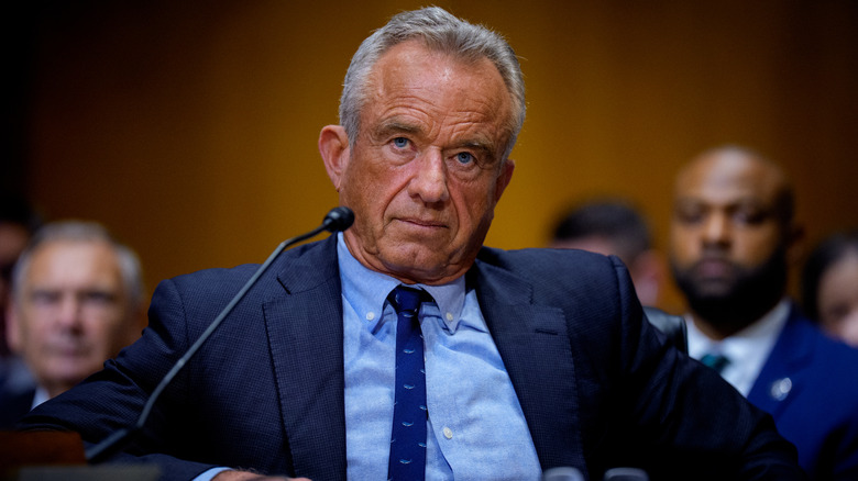 RFK Jr. behind a microphone at his Senate hearing in a navy blue suit