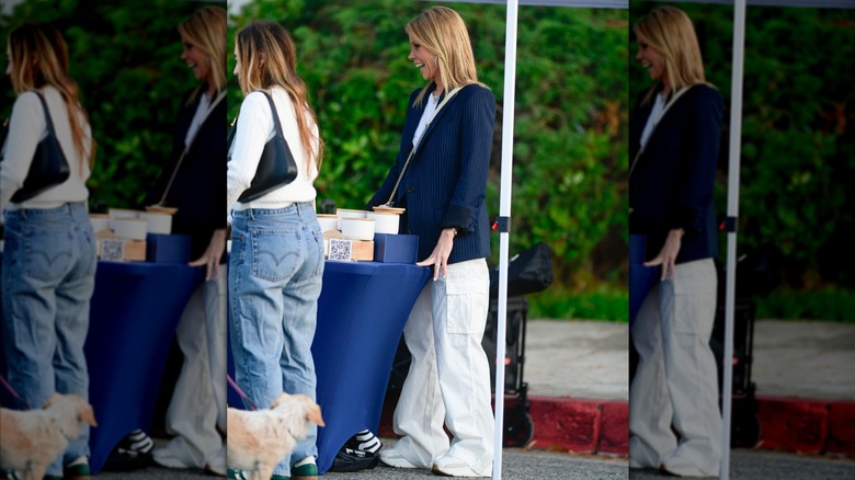 Candid photo of Cheryl Hines at an outdoor market wearing a blue blazer and ill-fitting white pants with chunky shoes