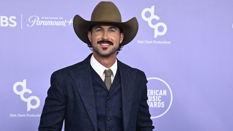 Riley Green smiling while wearing a navy suit and a big cowboy hat
