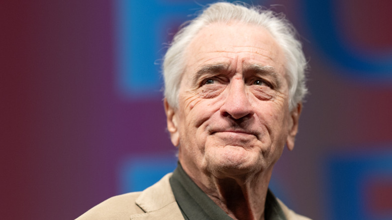 Robert De Niro looking pensive in a beige blazer with a dark green shirt underneath