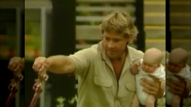 Steve Irwin holding his infant son, dangling meat over a crocodile