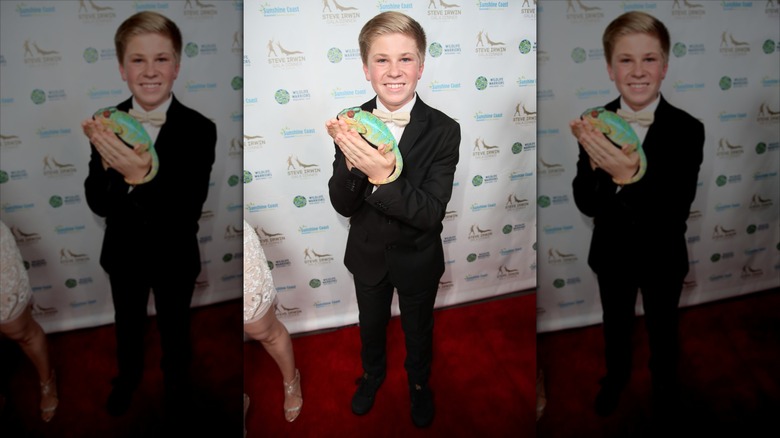Robert Irwin wearing a tux, holding a chameleon on a red carpet