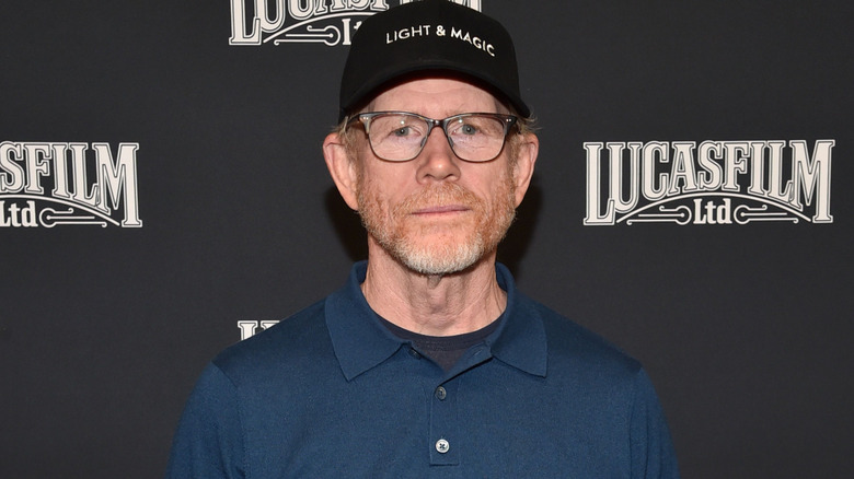 Ron Howard posing in front of a Lucasfilm backdrop in a black cap and glasses