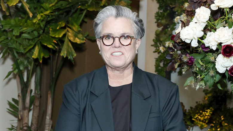 Rosie O'Donnell smiling in front of plants and flowers behind her