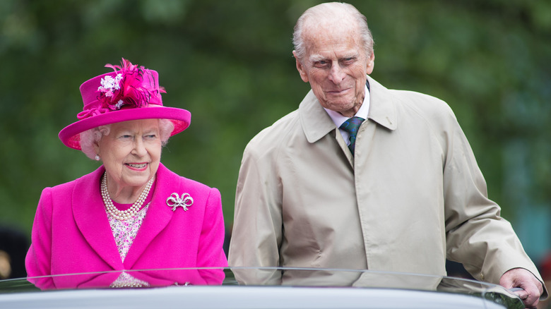 Queen Elizabeth II and Prince Philip smiling while sitting in an open-top car