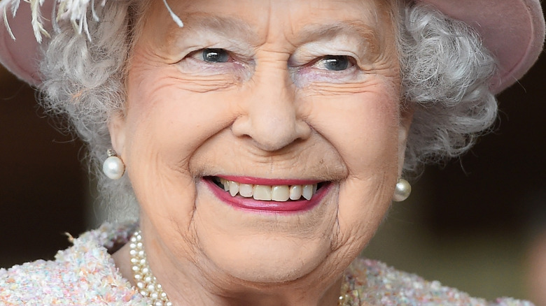 Queen Elizabeth with wide smile wearing pink hat with feather 