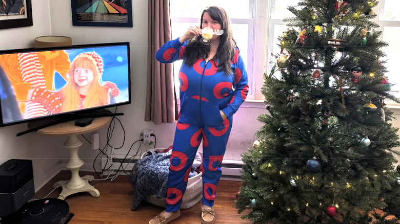 Ellen Latzen poses and drinks from a mug in front of a TV showing herself acting in "Christmas Vacation"