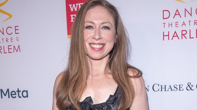 Chelsea Clinton smiling in front of a red carpet backdrop