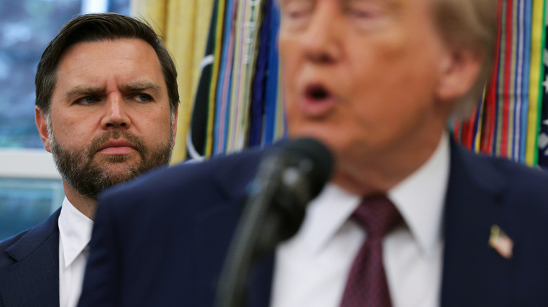 JD Vance giving someone side-eye from behind Donald Trump as he gives a speech