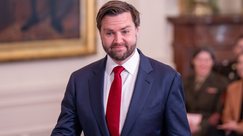 JD Vance looking slightly mortified in a navy suit with a red tie