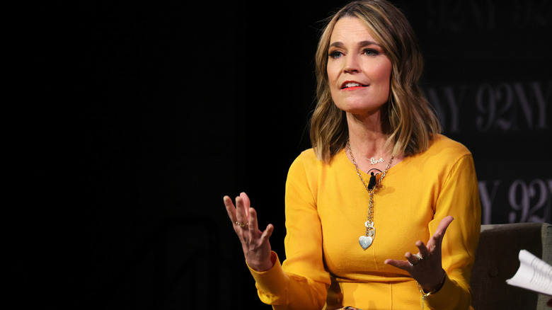 Savannah Guthrie gesturing with her hands while speaking onstage at an event in an orange dress