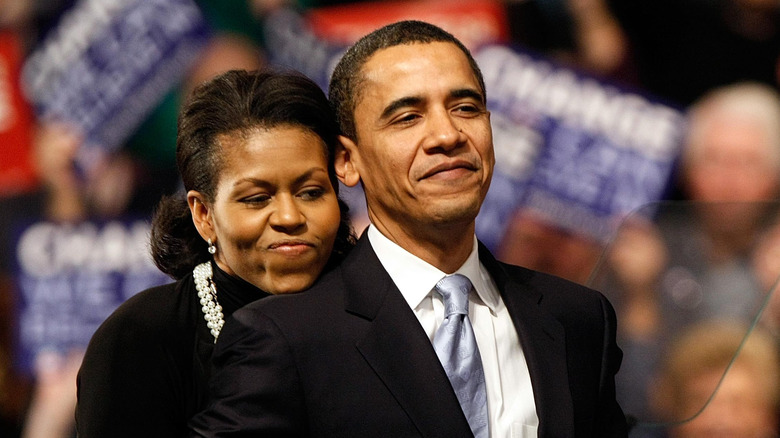 Michelle Obama hugging Barack Obama from behind.