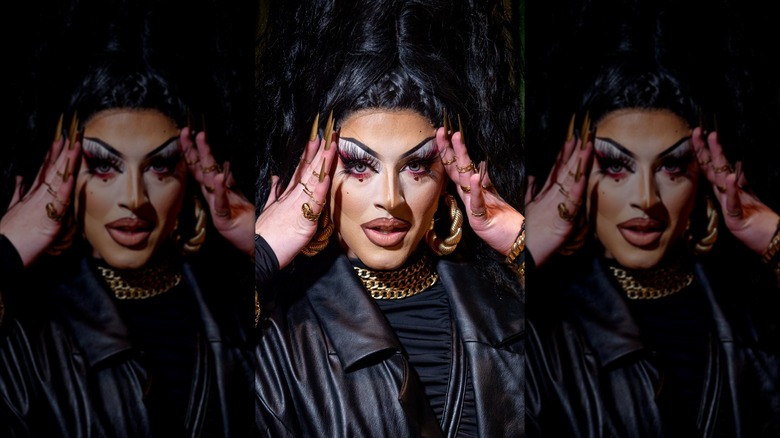 A closeup of Cherry Valentine holding her hands to her face, wearing a leather jacket