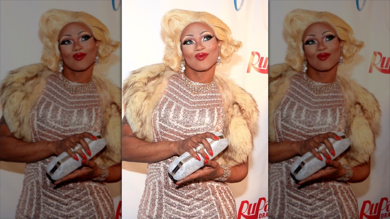 Chi Chi DeVayne in a blonde wig and fur shawl, clutching a sparkling purse