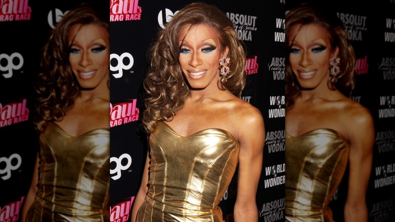 Sahara Davenport in a gold dress on a RuPaul's Drag Race step and repeat
