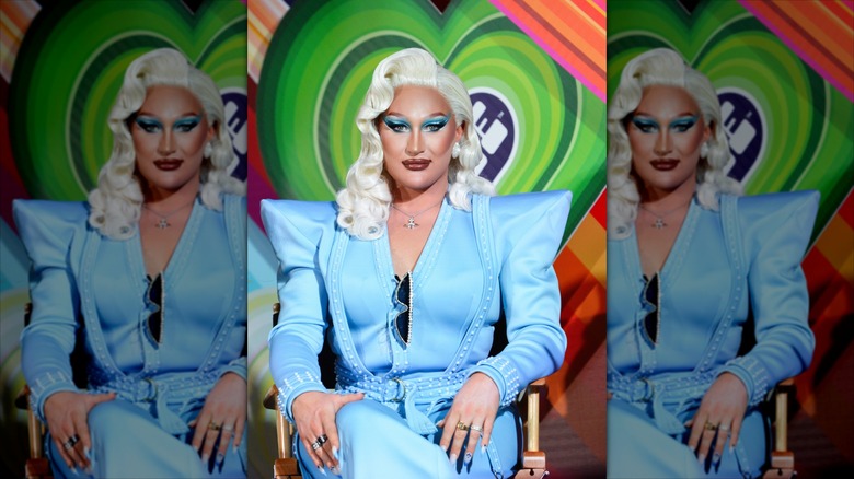 The Vivienne in a powder-blue suit, sitting in front of a green heart