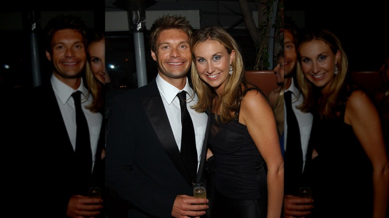 Ryan Seacrest wearing a black suit and tie and holding a glass of champagne next to Meredith Seacrest in a black dress