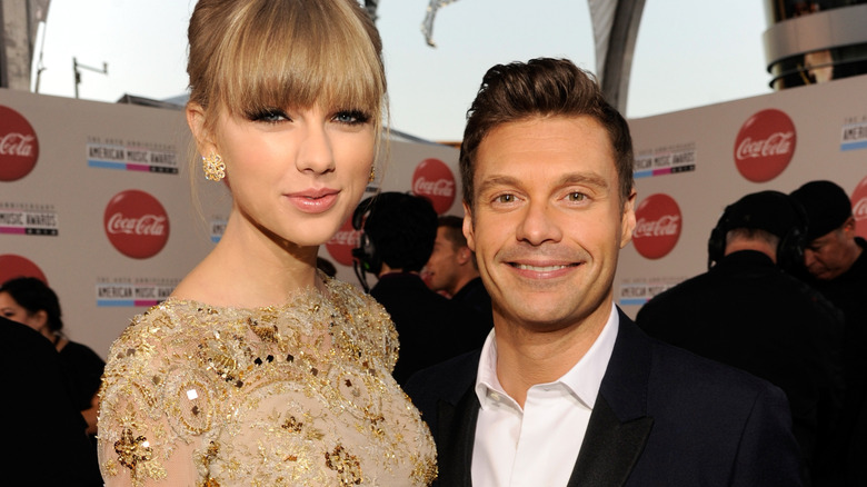 Ryan Seacrest and Taylor Swift posing and smiling at the American Music Awards on the red carpet.
