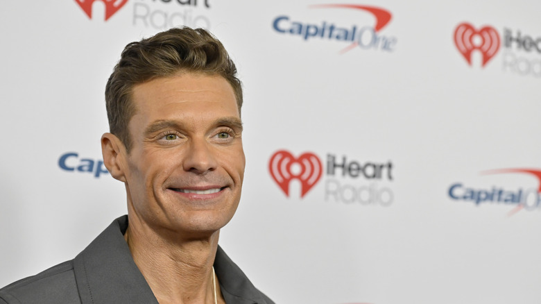 Ryan Seacrest smiling in a grey blazer