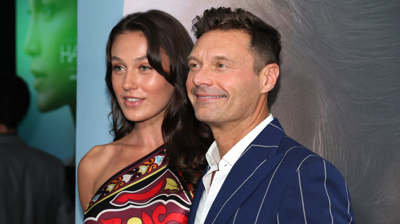 Aubrey Paige in a colorful dress posing with Ryan Seacrest in a striped suit.