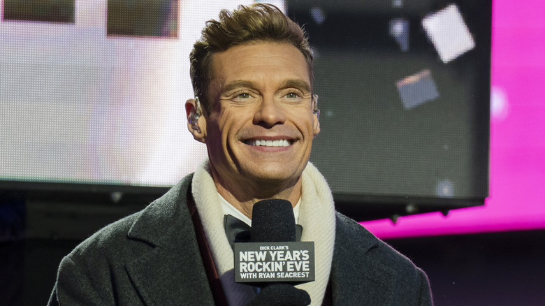 Ryan Seacrest wearing a coat and holding up a microphone