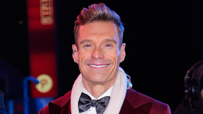 Ryan Seacrest smiling in a red tuxedo on NYE 2025