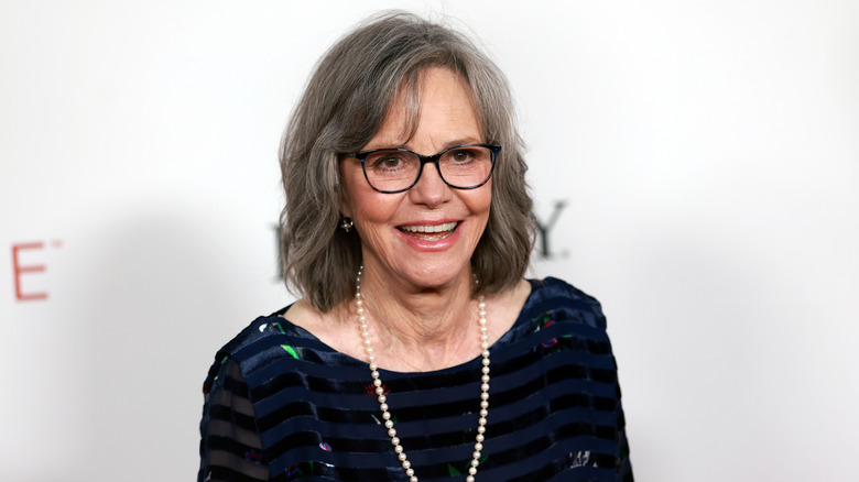 Sally Field wearing a striped dress, glasses, and pearls