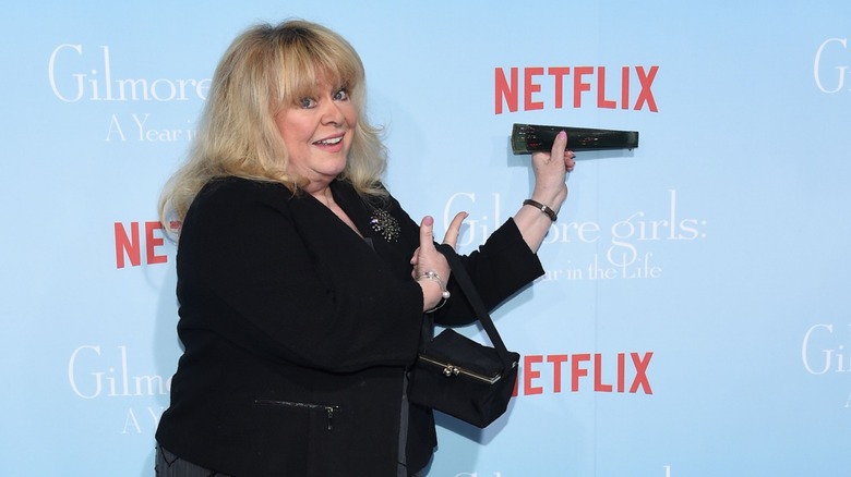 Sally Struthers pictured wearing a black cardigan and holding a black fan