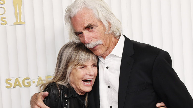 Katharine Ross laughing as Sam Elliott rests his head on the top of her head