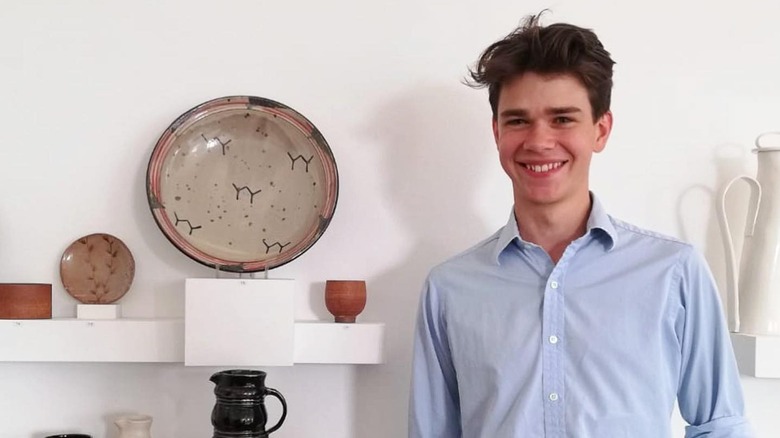 Samuel Chatto smiling next to pottery on shelves