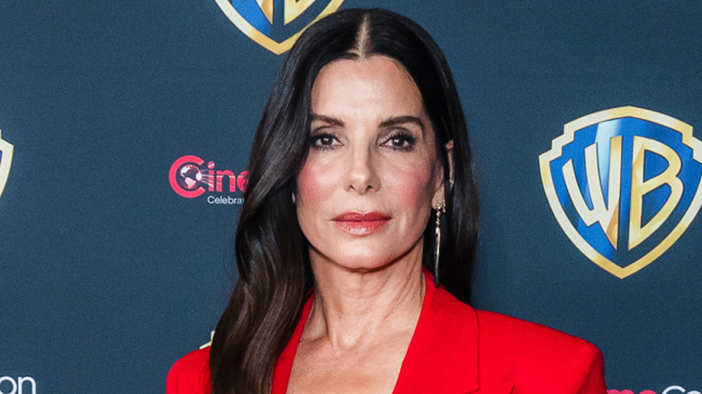 Sandra Bullock posing at an event in a red blazer with neutral expression