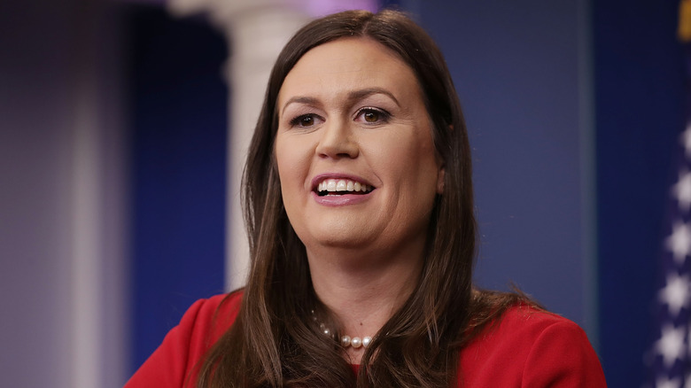 Sarah Huckabee Sanders smiles wearing pearls and a red outfit