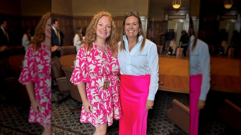 Sarah Huckabee Sanders wearing a white button-up shirt and pink skirt next to Cortney Kennedy who's also wearing a pink dress.