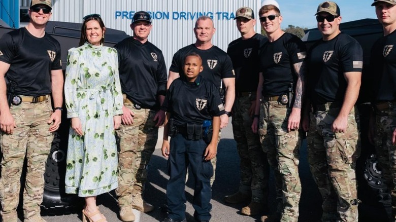 Sarah Huckabee Sanders poses in a long dress, surrounded by police (2025)